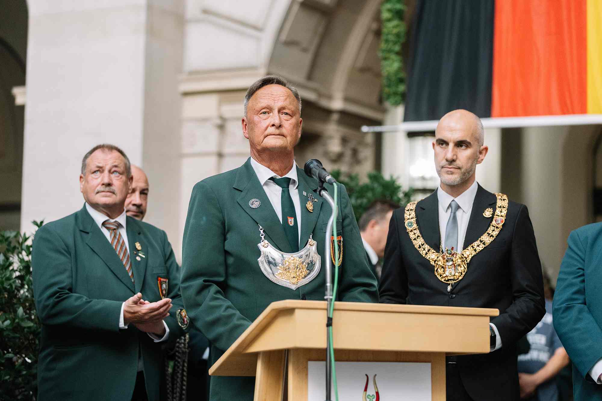 Schützenfest Hannover 2026 Hannovers Oberbürgermeister Belit Onay (rechts im Bild). Er trägt die prachtvolle, goldene Amtskette des Oberbürgermeisters von Hannover um die Schultern. Links von ihm steht ein Schützenkönig am Rednerpult. Er trägt eine traditionelle dunkelgrüne Schützenjacke, eine passende grüne Vereinskrawatte und die große, silberne Königskette (Schützenkette) um den Hals.